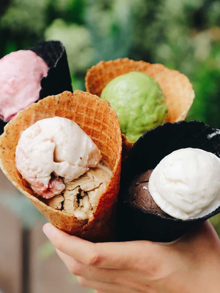 Hand holding multiple ice creams in cones